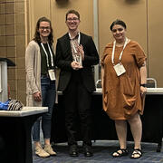 Photo of three people, with Gabe in the center holding a glass trophy