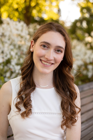 A smiling young woman with long brown hair and wearing a white sleeveless top.