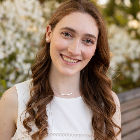 A smiling young woman with long brown hair and wearing a white sleeveless top.