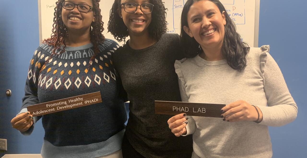 Picture of Ariana Rivens, Dr. Janelle Billingsley, and Andrea Negrete posing with the PHAD Lab signs 