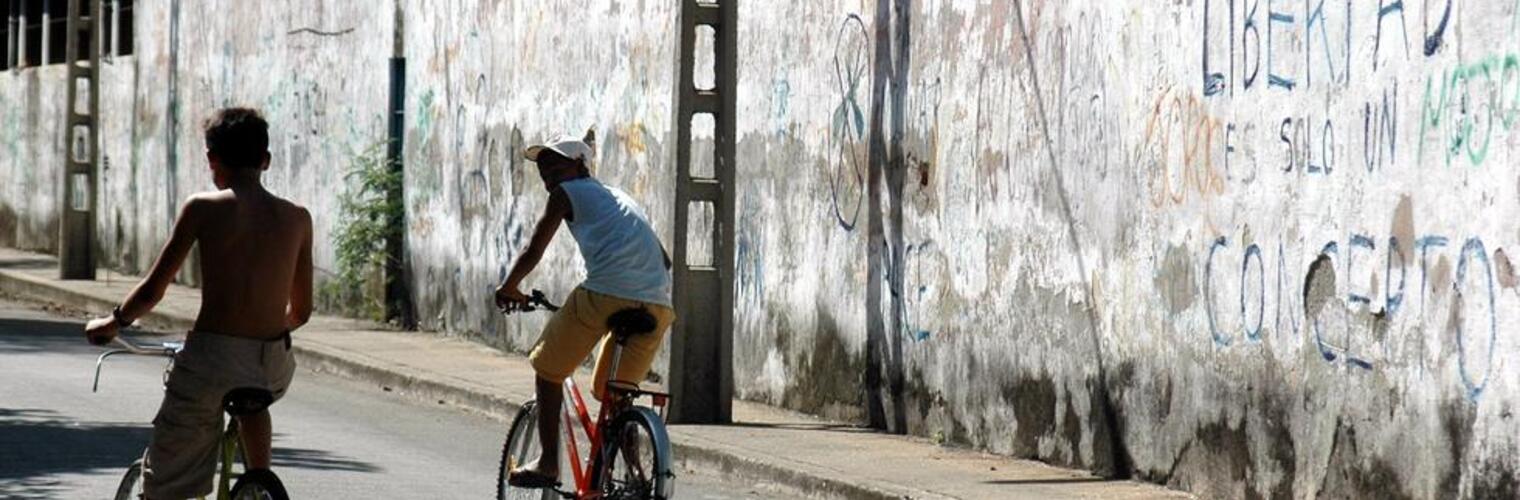 Two kids on bikes riding alongside a graffiti-ed wall