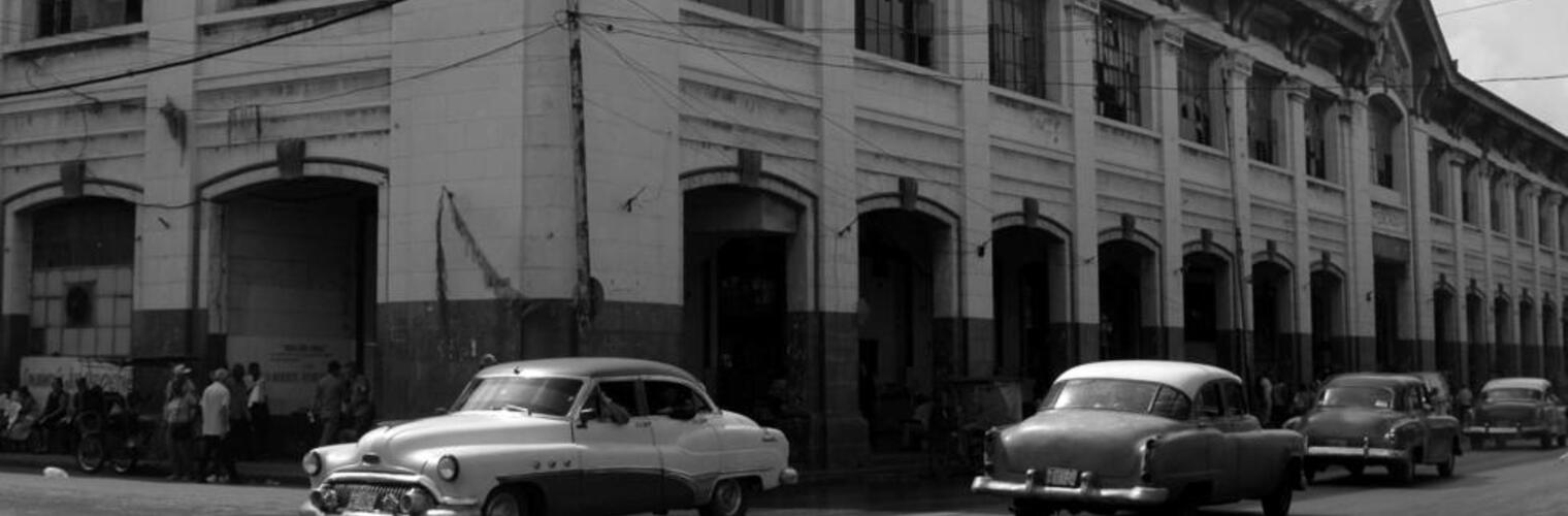 A building in Cuba with cars out front, photographed in black and white.